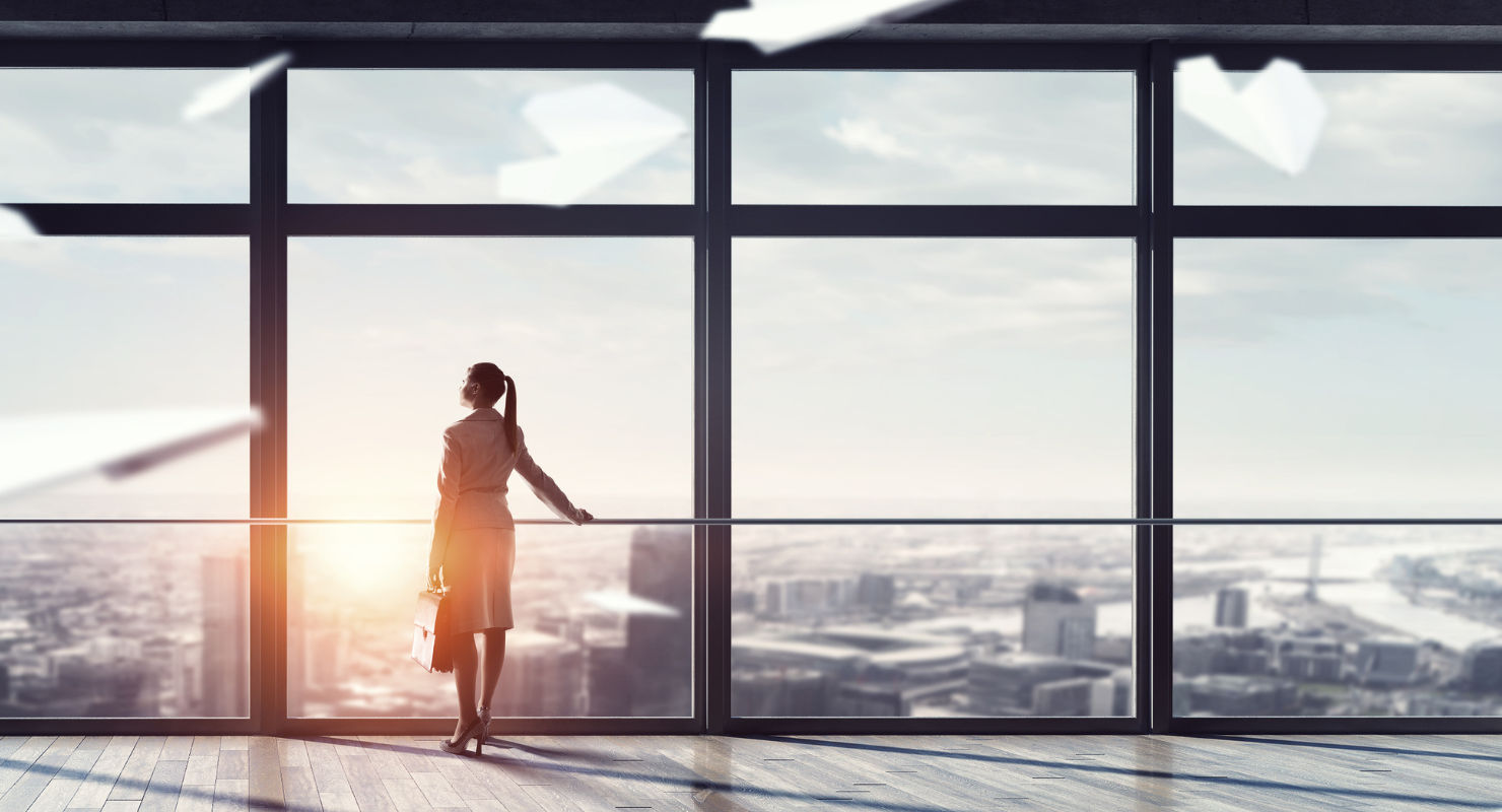 a woman stands in front of a large window looking out over a city
